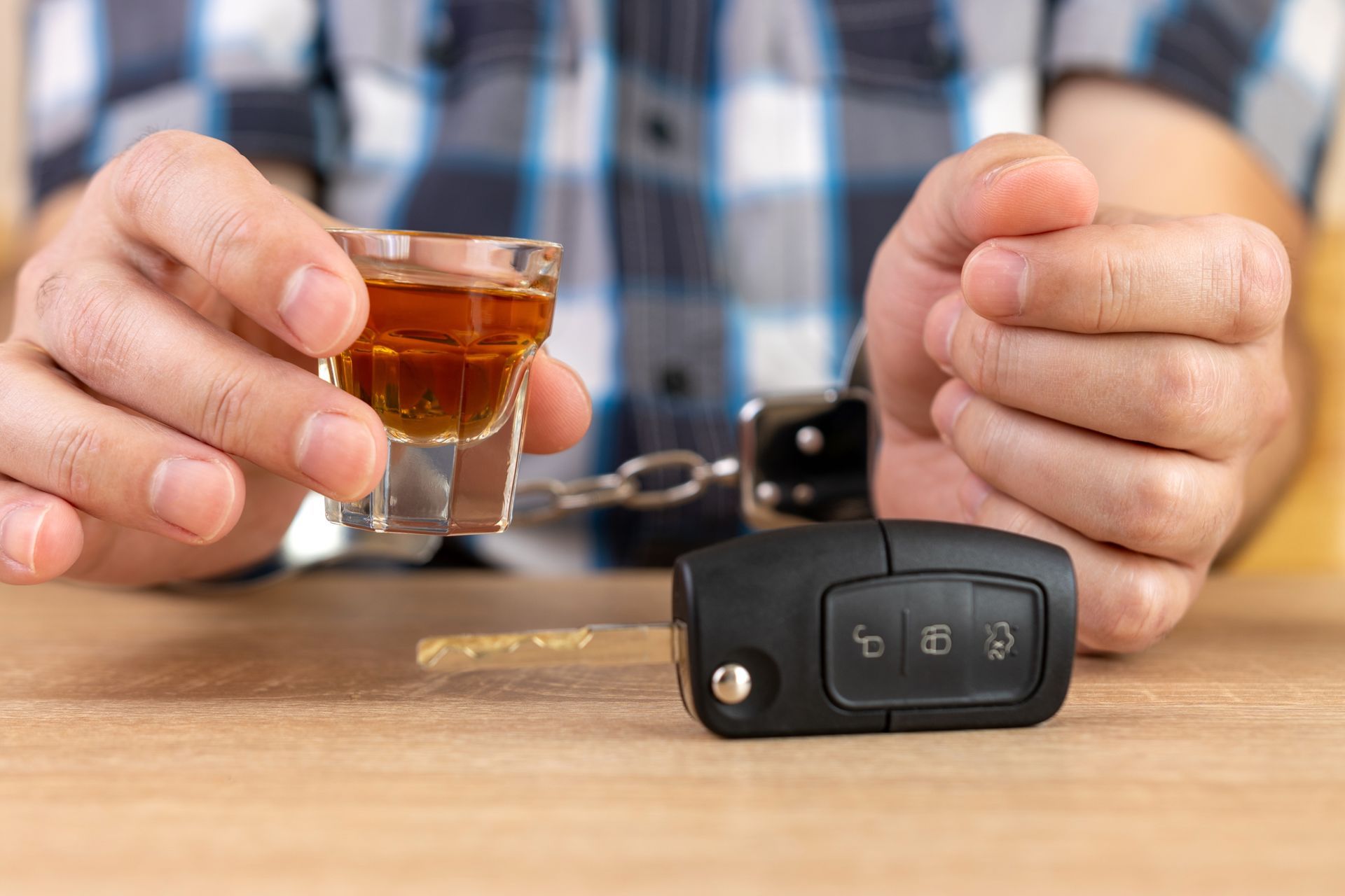 Person holding a glass of liquor beside a car key fob, suggesting drunk driving awareness