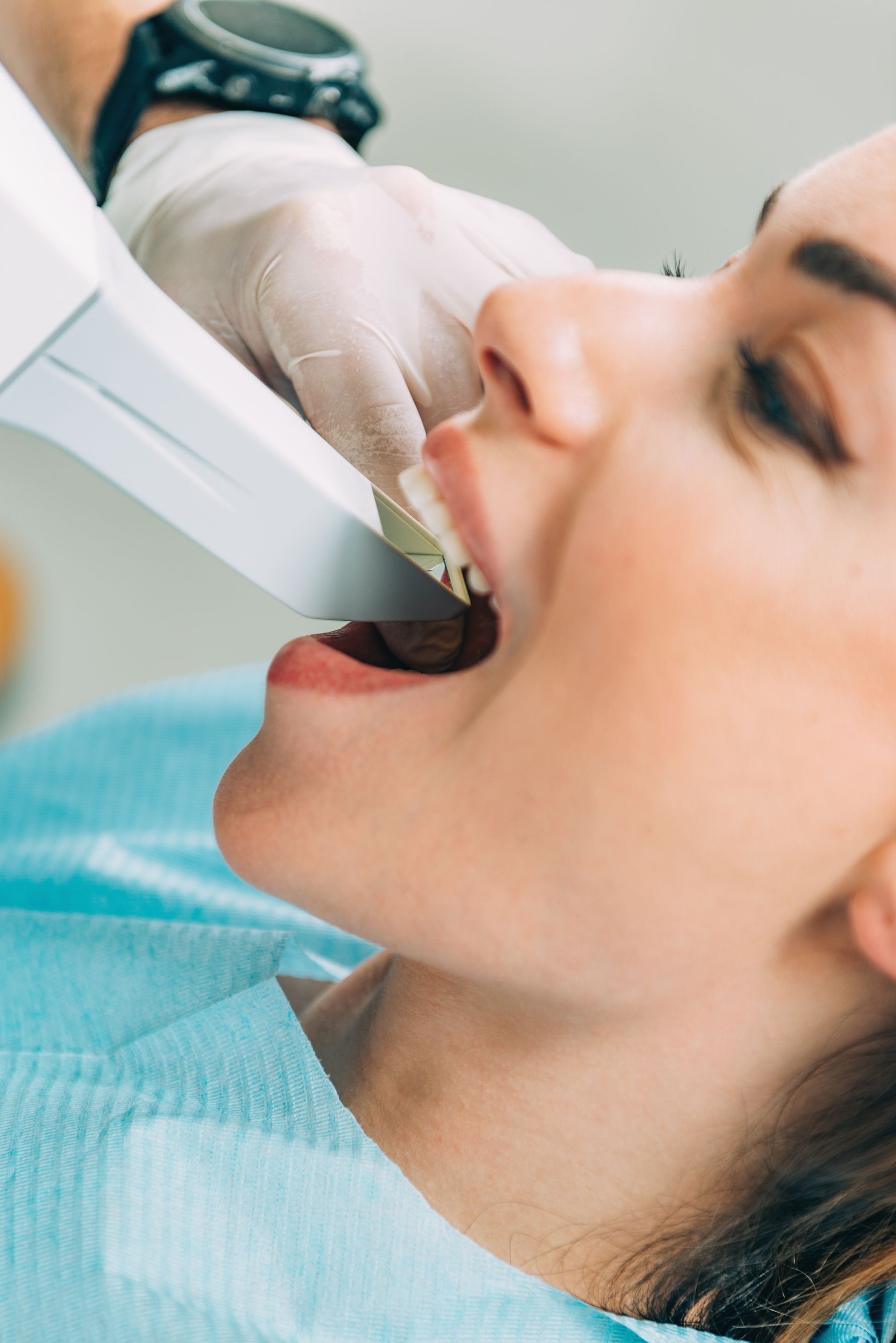 Dentist in gloves uses a handheld scanner on a reclined patient during a cosmetic dentistry visit. Dentist in gloves uses a handheld scanner on a reclined patient during a cosmetic dentistry visit.