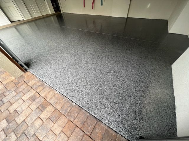 Garage floor with speckled gray epoxy coating, leading from brick entryway.