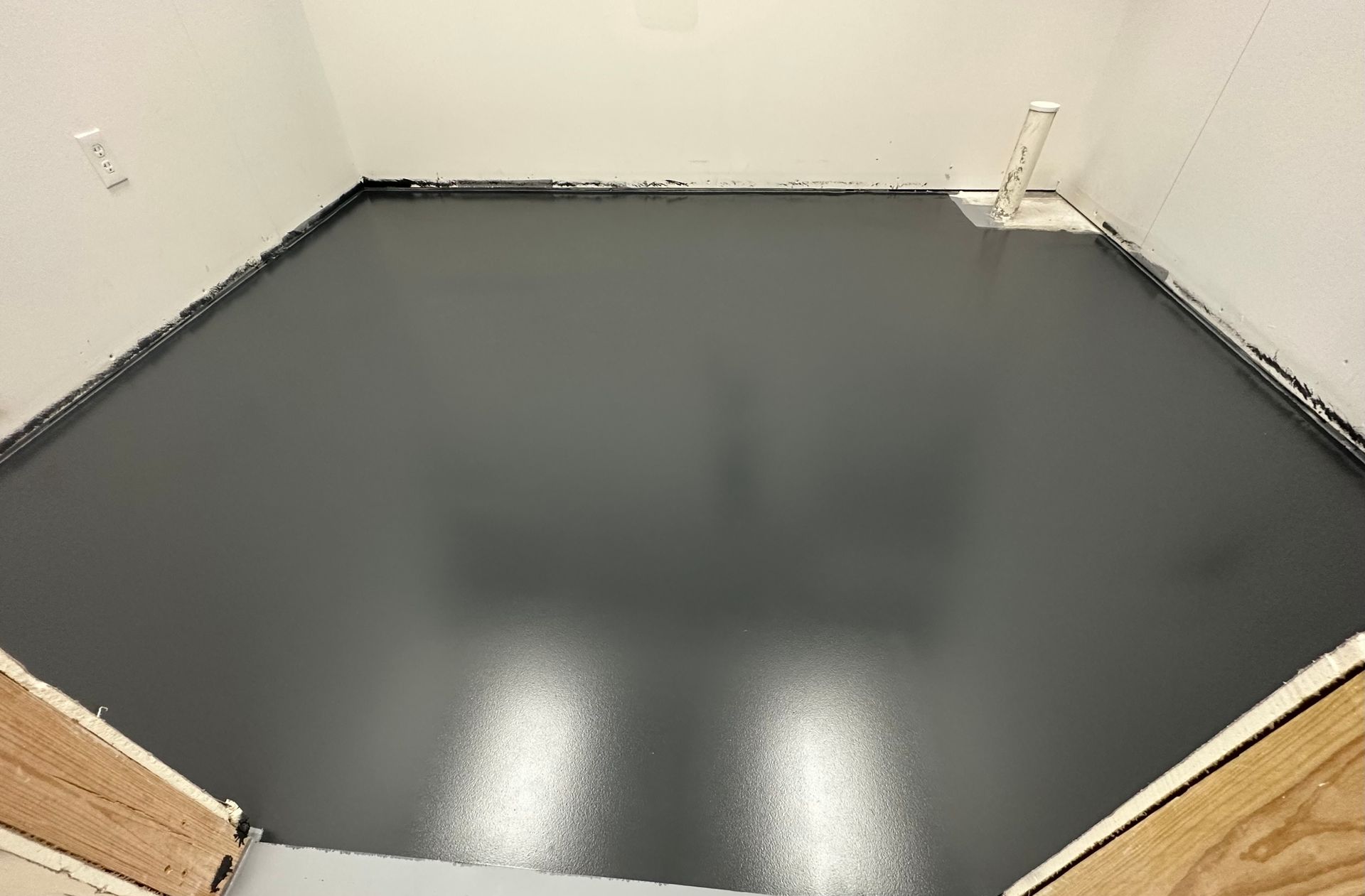 Dark gray epoxy floor in a room, viewed from above, with white walls and unfinished wood frame visible.