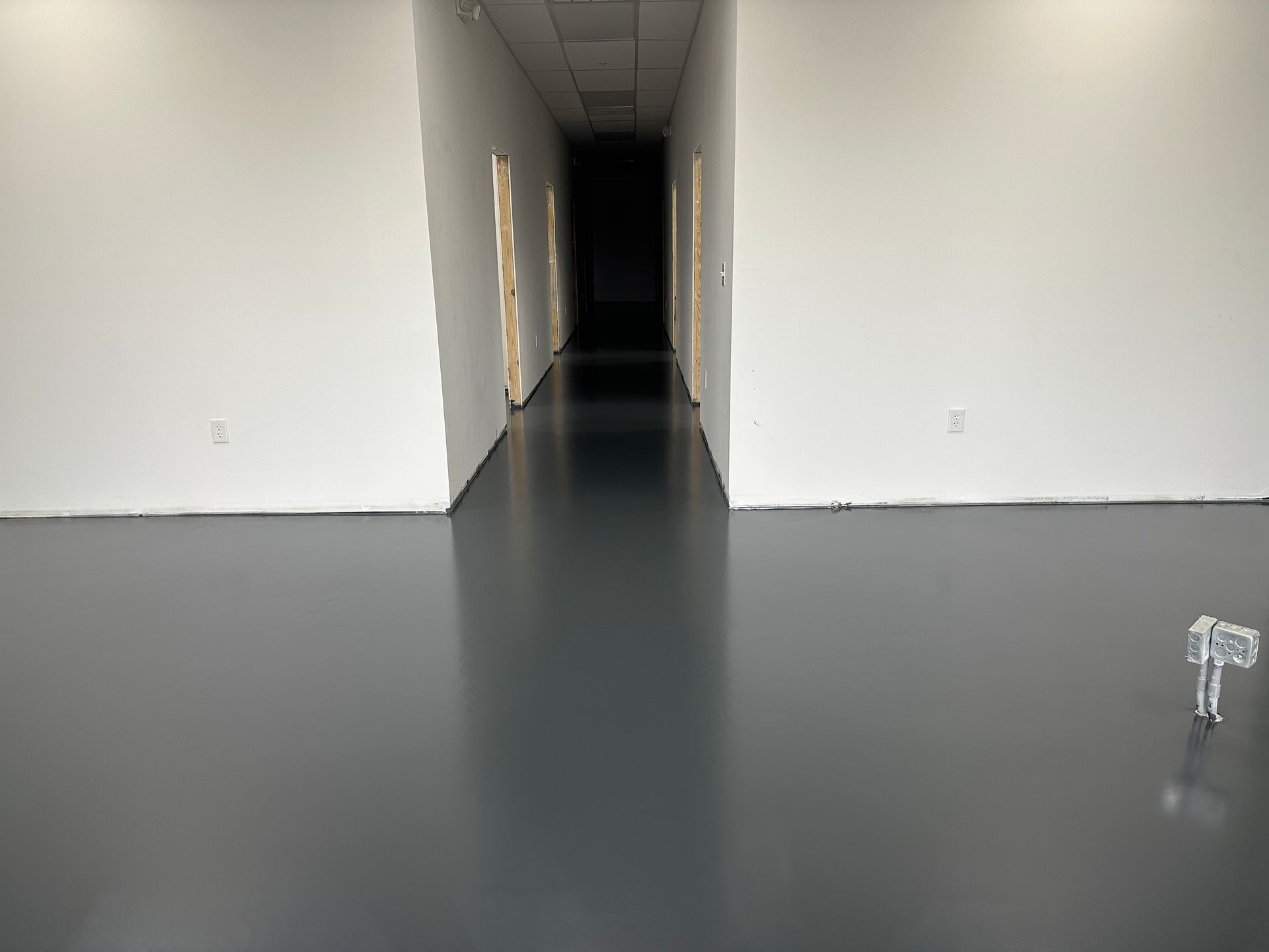 Empty, long hallway with dark, reflective floor and white walls. Distant doorways visible.