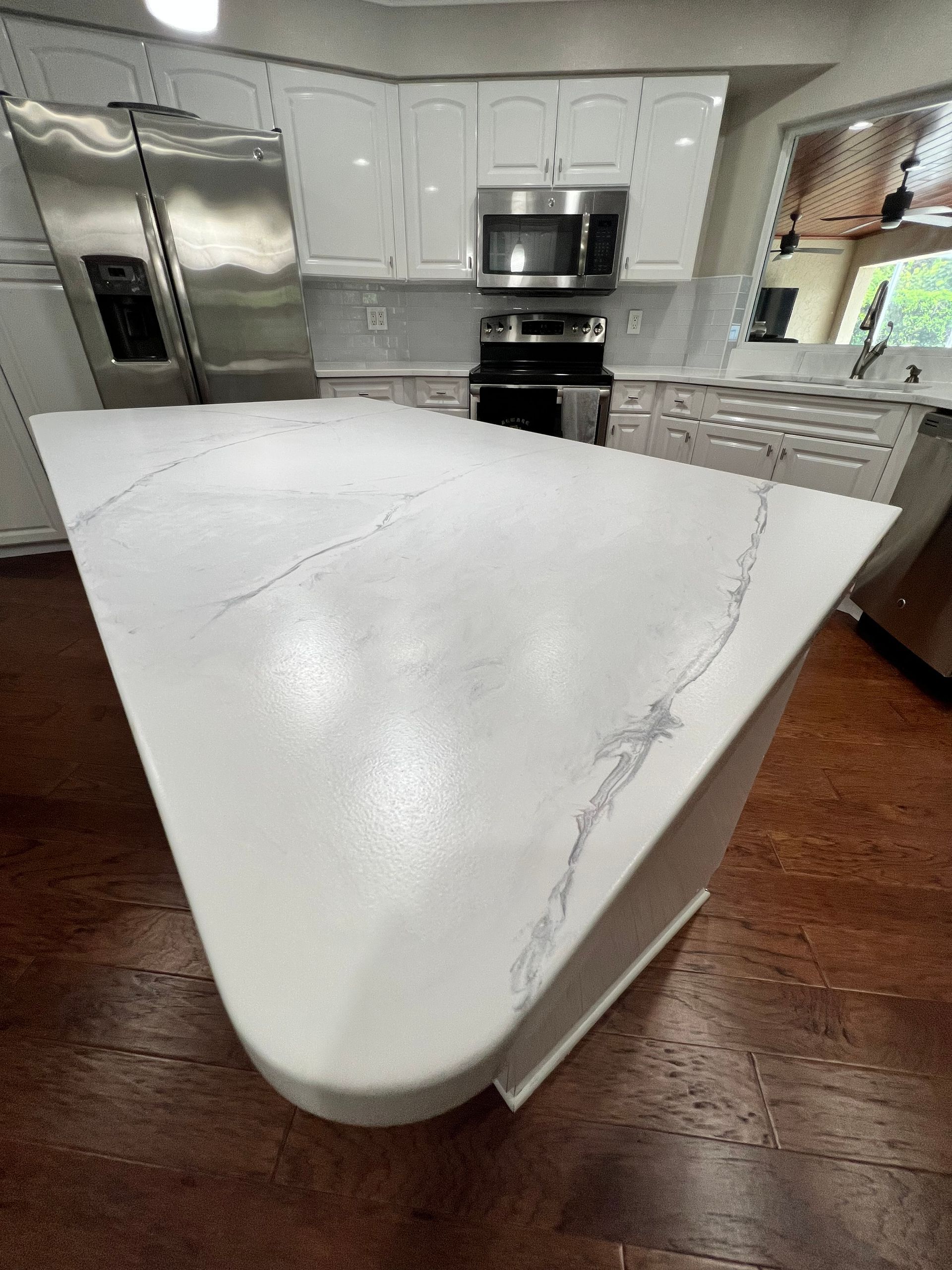 White kitchen island with marble-look countertop and white cabinets. Stainless steel appliances.