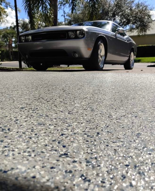 Silver Dodge Challenger parked on a speckled garage floor, sunny outdoor setting.
