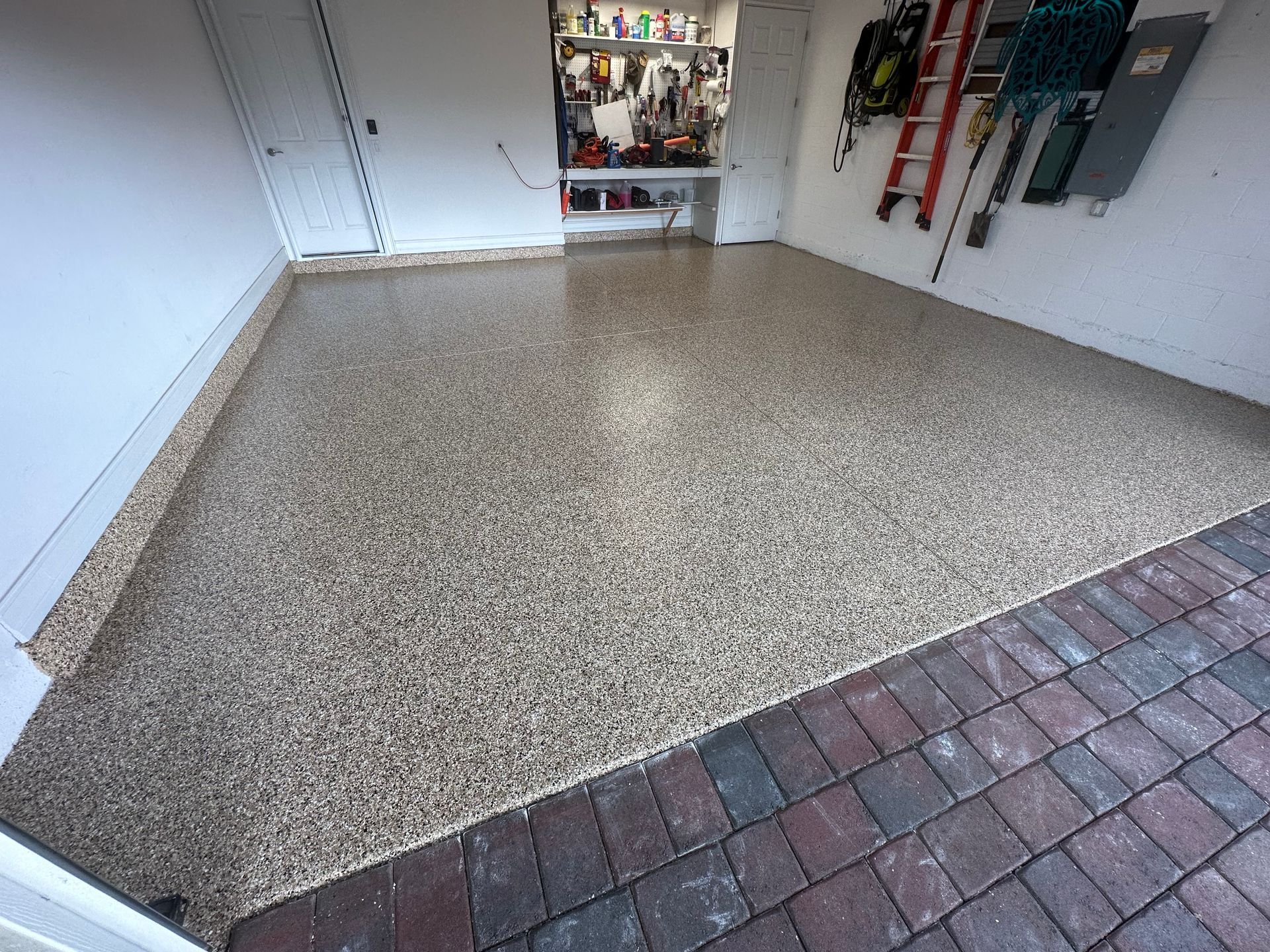 Garage floor with a speckled epoxy coating, adjacent to a brick driveway.