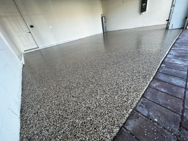 Epoxy-coated garage floor with flecks of color; adjacent to brick pavers and white walls.