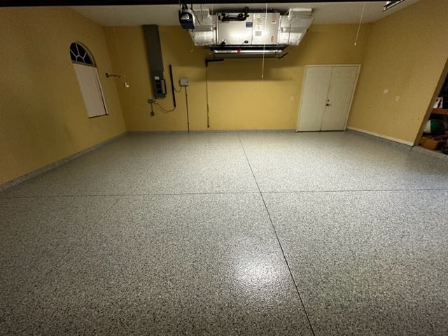 Empty garage with a gray speckled epoxy floor, beige walls, and overhead mechanicals.