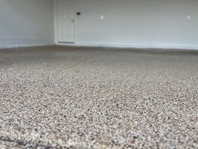 Close-up of a speckled, textured floor in a bright, empty room. A white door is visible in the background.