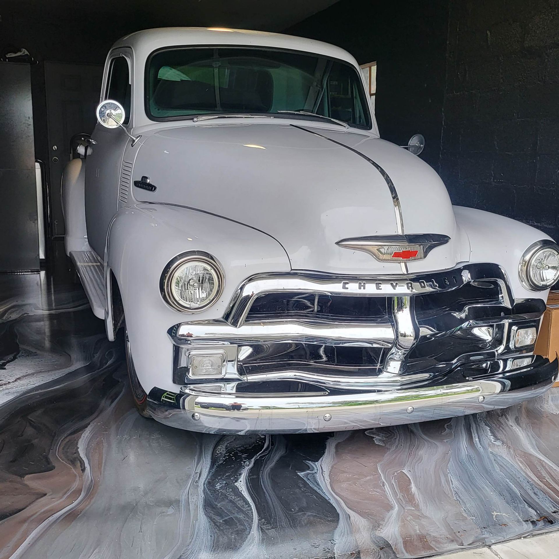 Vintage white Chevrolet pickup truck parked on a metallic epoxy floor, chrome accents.