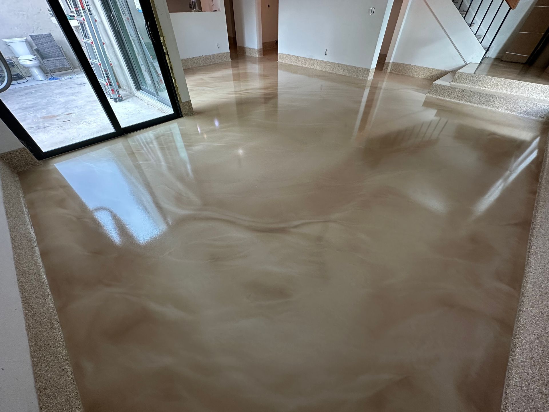 Shiny, swirled, metallic-looking epoxy floor in shades of brown and beige. A glass door and stairs are visible.