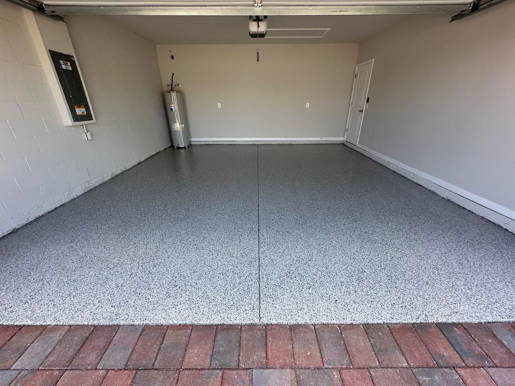 Empty garage with gray speckled epoxy floor and brick entryway.