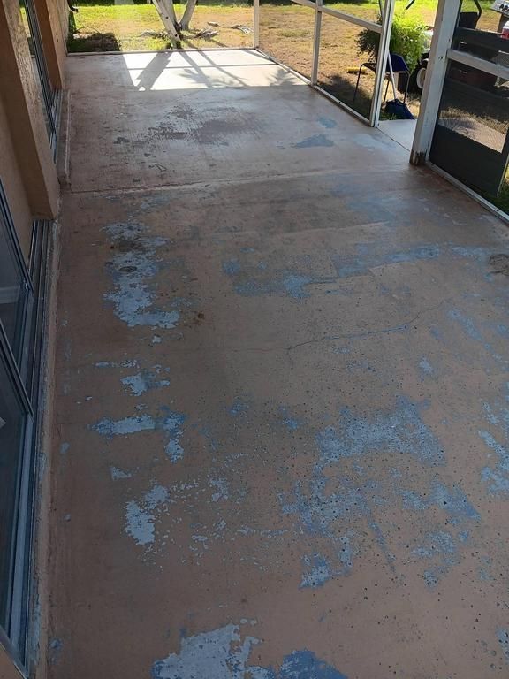 Brown concrete patio with peeling paint, adjacent to a house and screened enclosure.