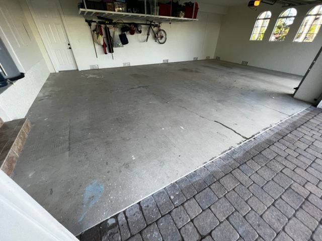 Garage interior with concrete floor, overhead storage, and a brick driveway.