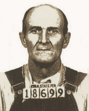 Black-and-white mugshot of a man wearing a numbered placard, facing forward against a plain background