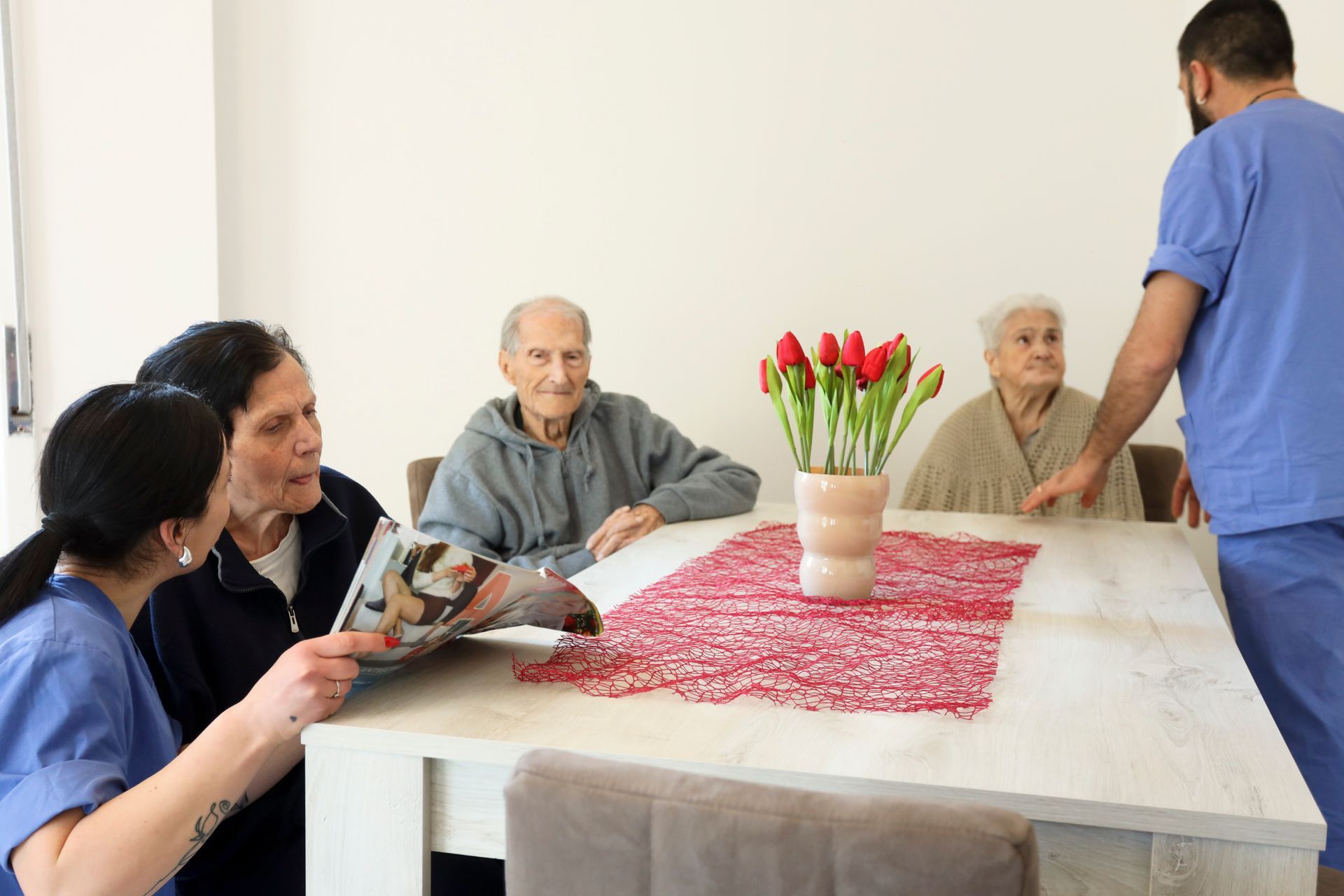 Due assistenti mostrano una rivista a tre anziani seduti a un tavolo con dei fiori.