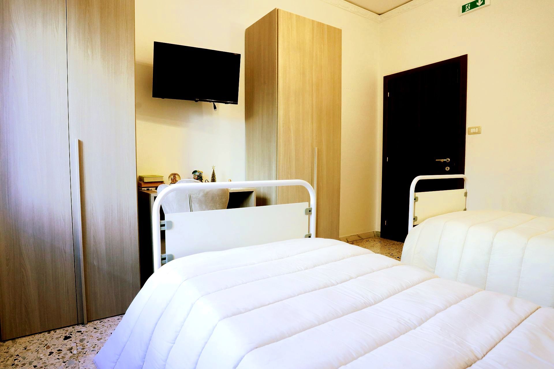 Stanza d'ospedale con due letti, TV e armadi.
