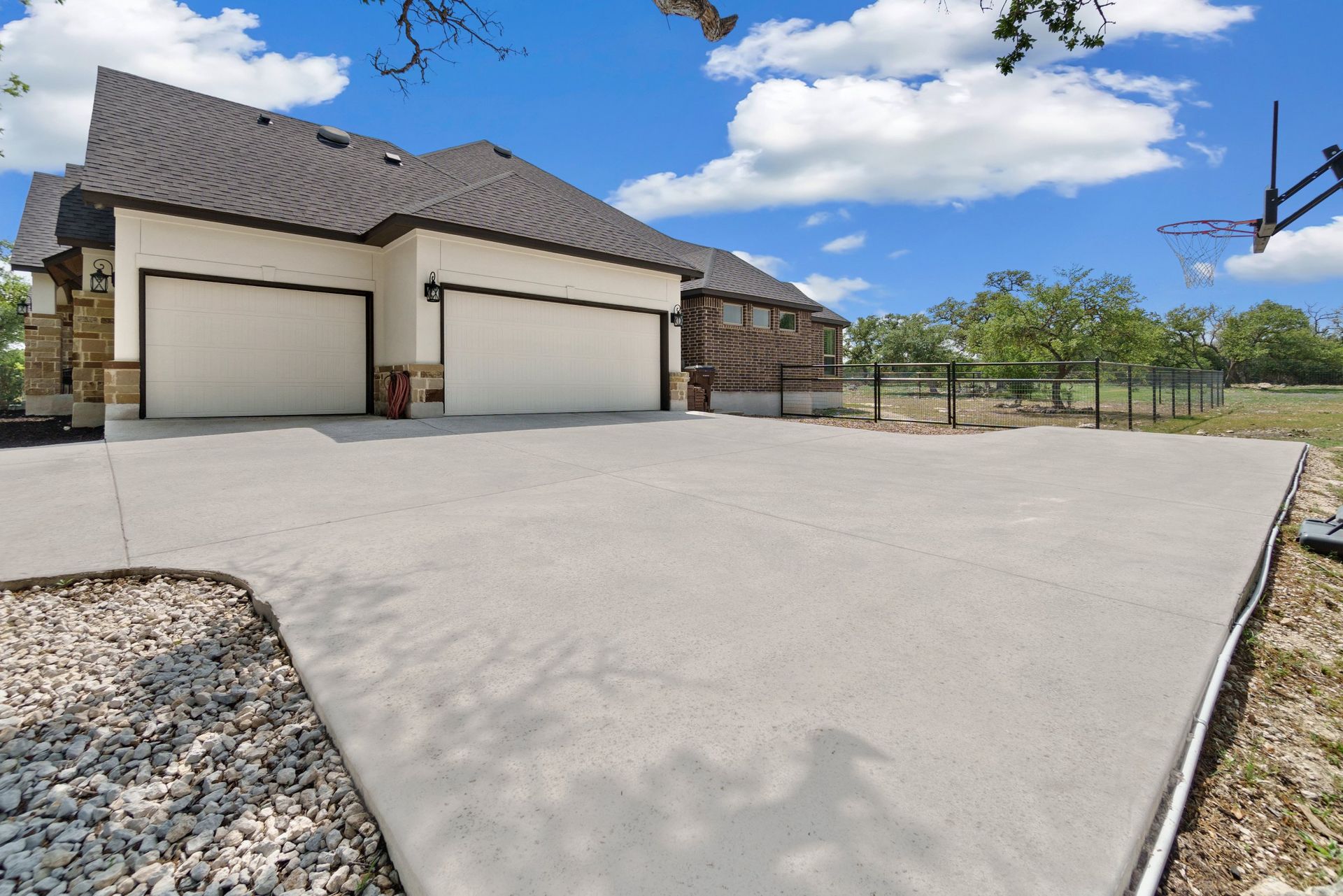 Modern house with three garage doors and a large concrete driveway under a blue sky