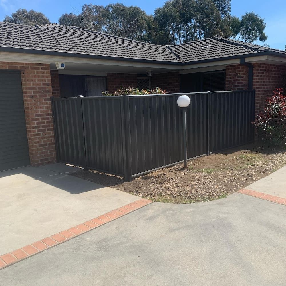 A Black Fence is in Front of a Brick House — CLF Landscaping In Hawker, ACT
