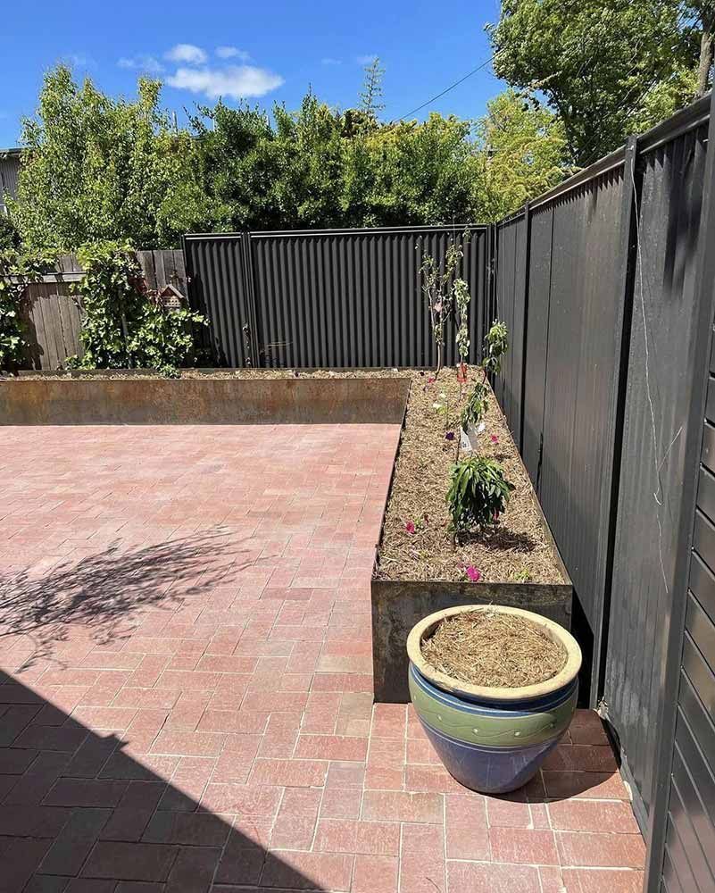 Backyard With a Brick Patio, a Planter Box, a Large Pot, and a Dark Fence — CLF Landscapes in Tuggeranong, ACT