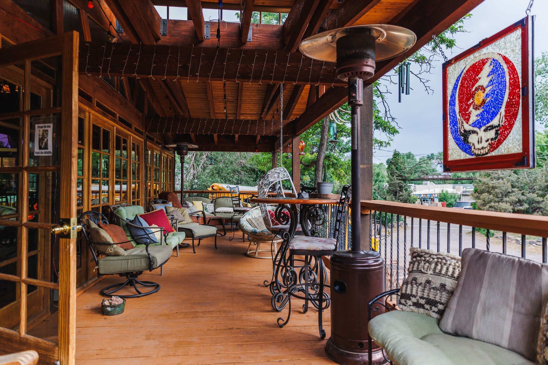A covered wooden deck features patio furniture, a tall outdoor heater, and a colorful Steal Your Face sign hanging nearby.