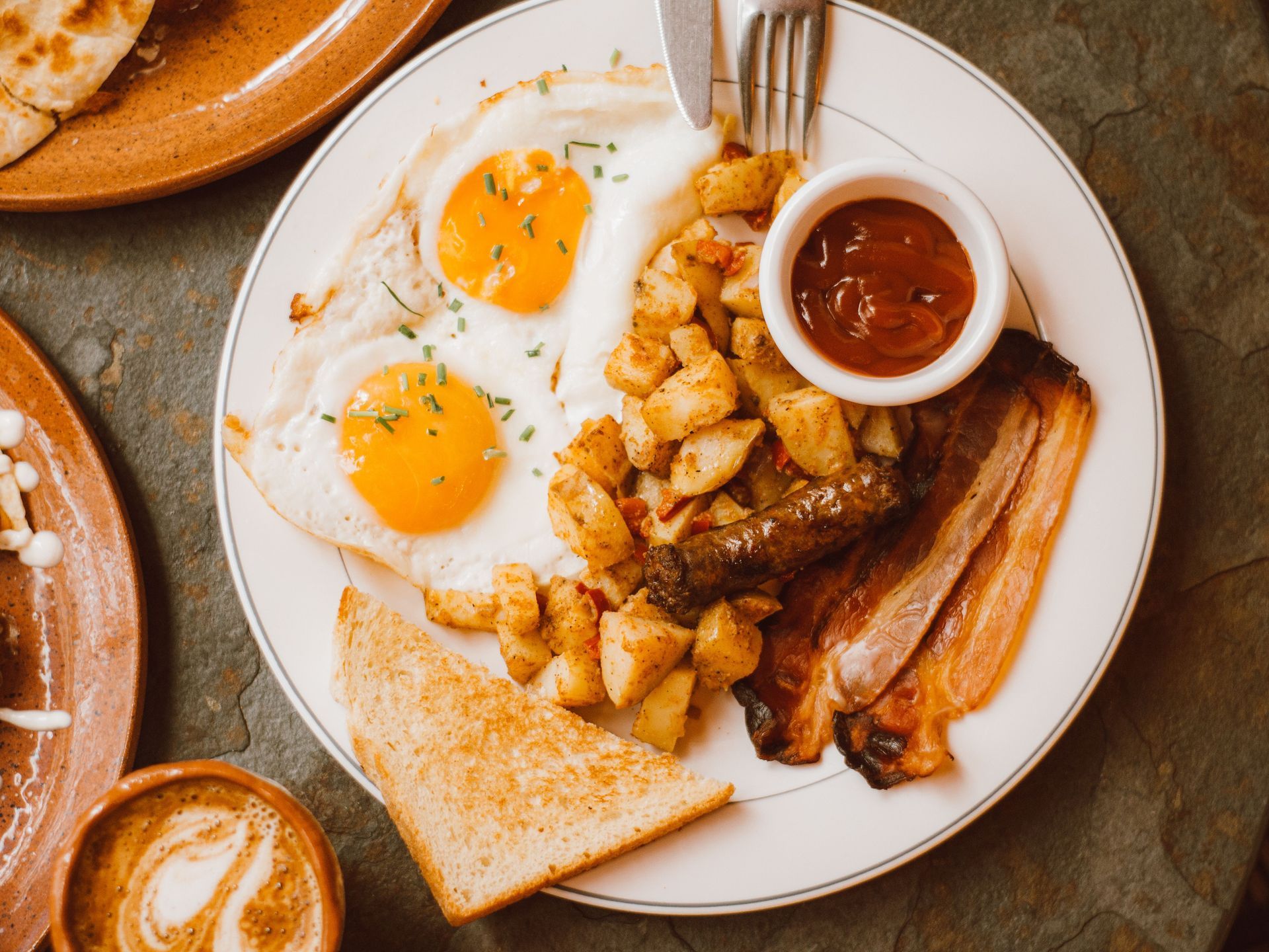 Breakfast plate with fried eggs, bacon, potatoes, toast, and a side of sauce
