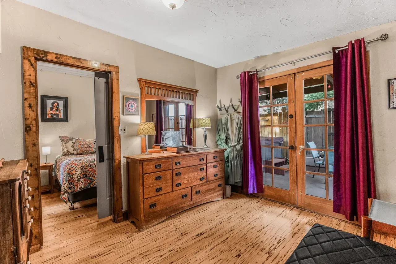 A bedroom with light wood floors, a wooden dresser with a mirror, a doorway to another room, and a glass patio door.