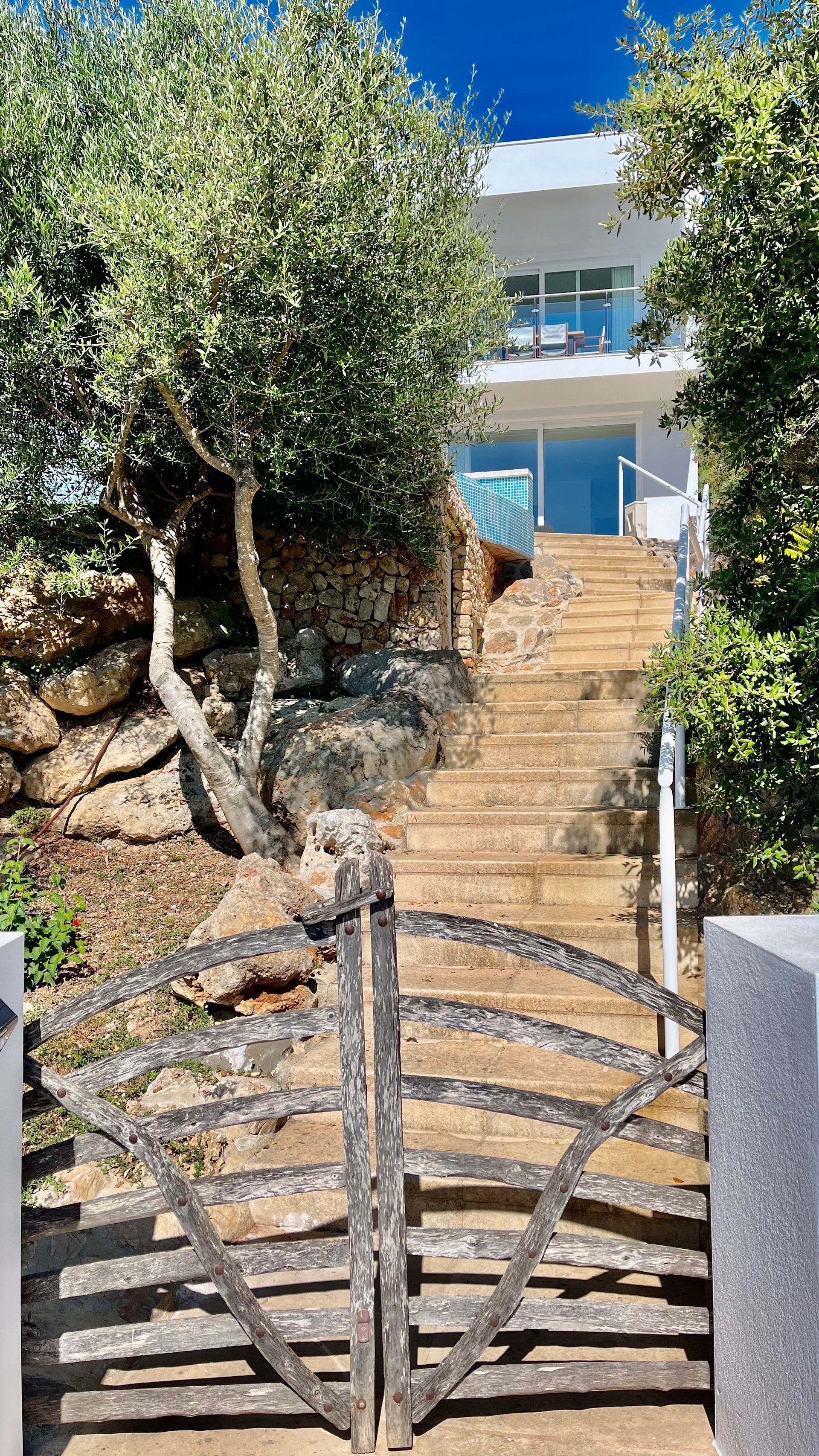 Una puerta de hierro conduce a unos escalones de piedra que suben a un edificio blanco con un balcón azul.