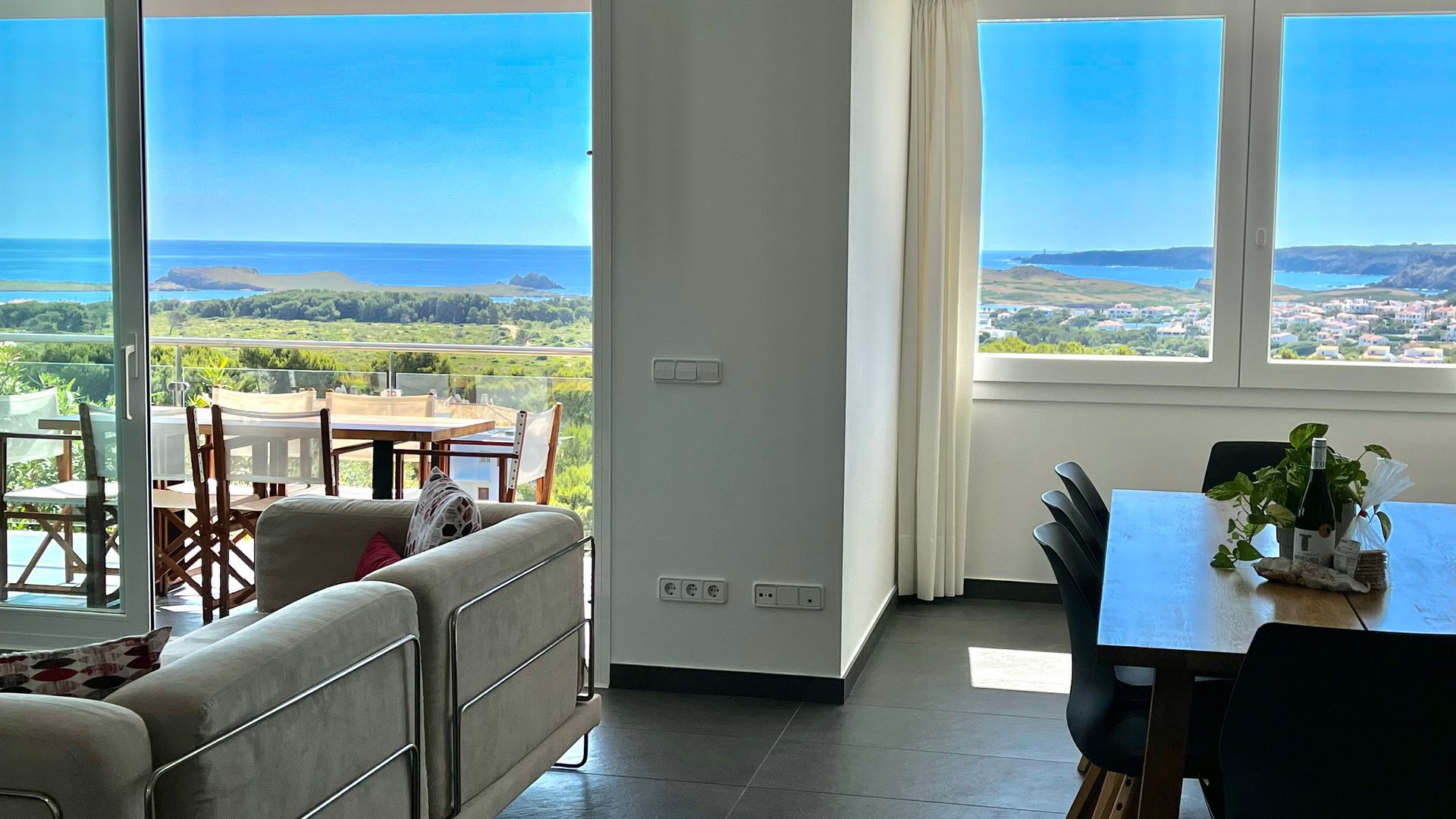 Luminosa sala de estar con vista al mar; mesa de comedor, sofá y amplios ventanales.