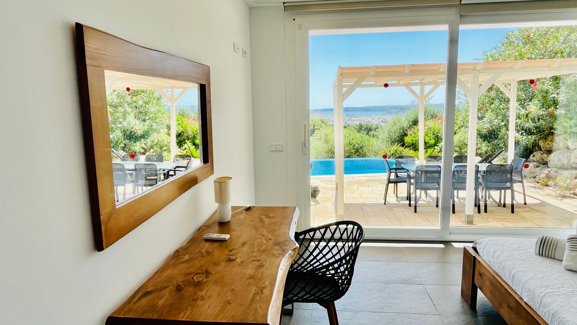 Dormitorio con escritorio y gran espejo con vista a una piscina y comedor al aire libre con vista panorámica.