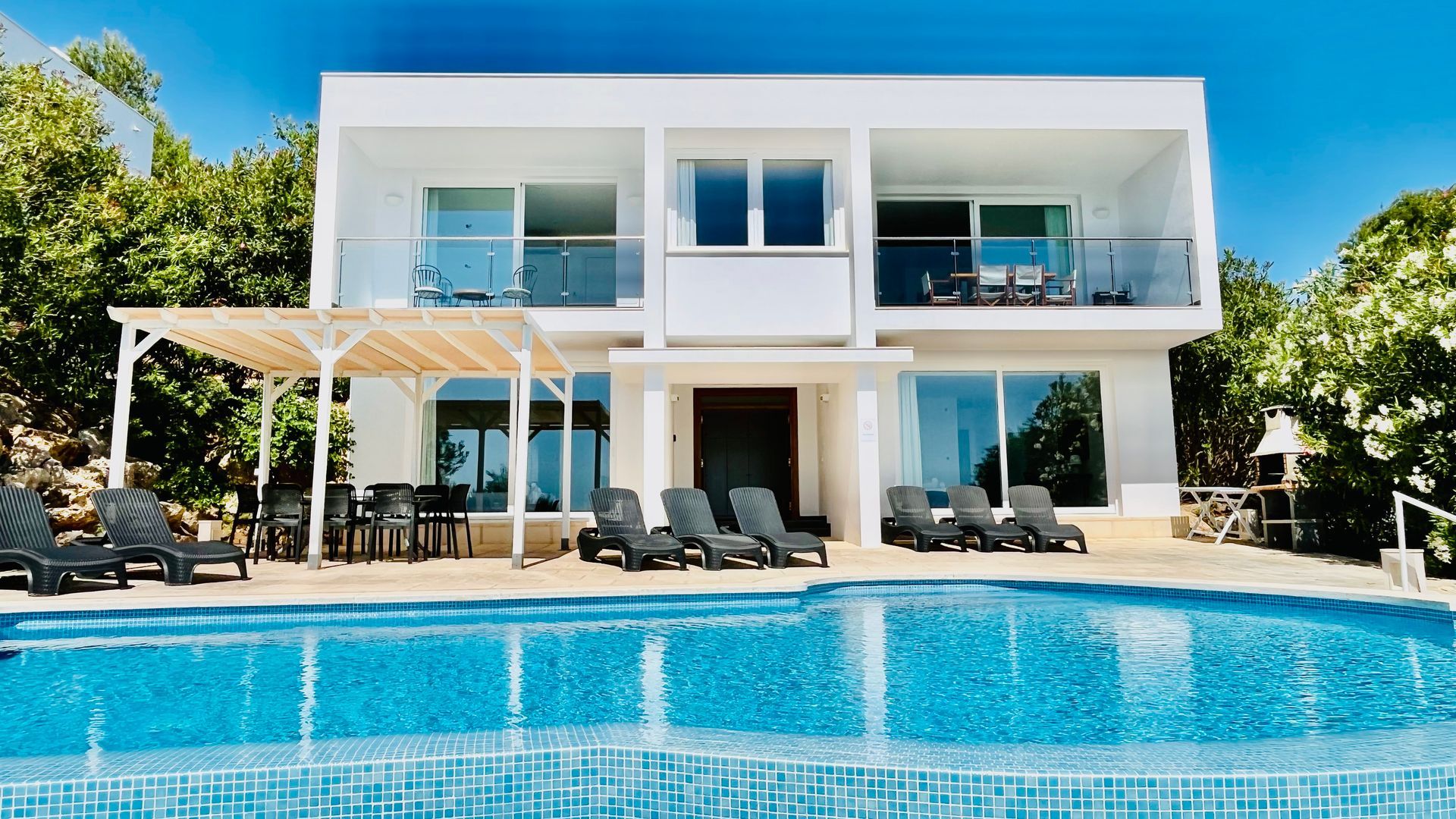 Villa moderna blanca con piscina y tumbonas.