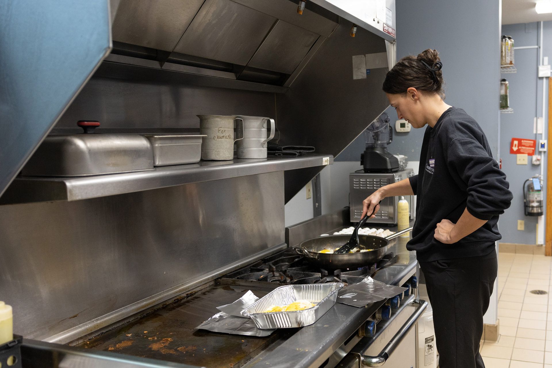 Woman cooking over a stove in a commercial kitchen. She's stirring food in a pan.
