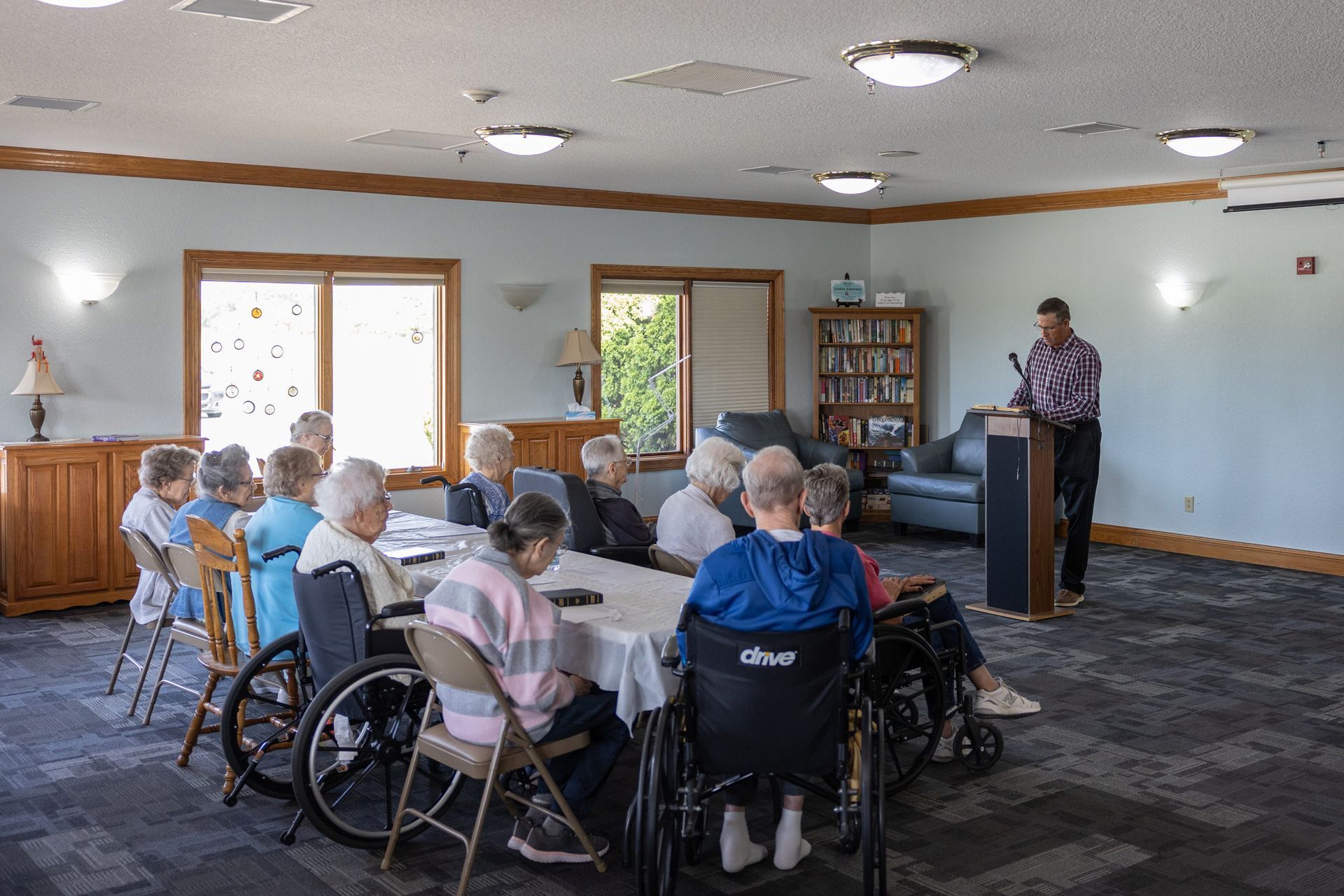 A man speaks at a podium to a group of seated seniors in a community room.