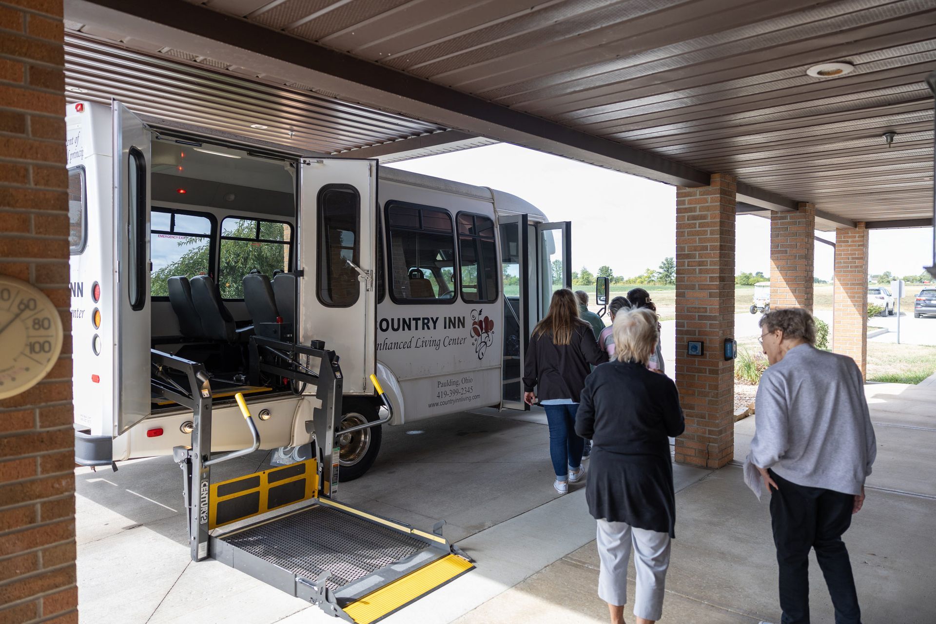 People boarding a transport bus with a wheelchair lift under a covered area.