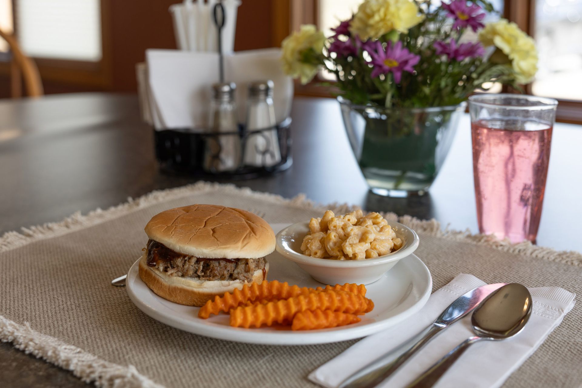 Plate with pulled pork sandwich, mac and cheese, sweet potato fries, and pink drink.