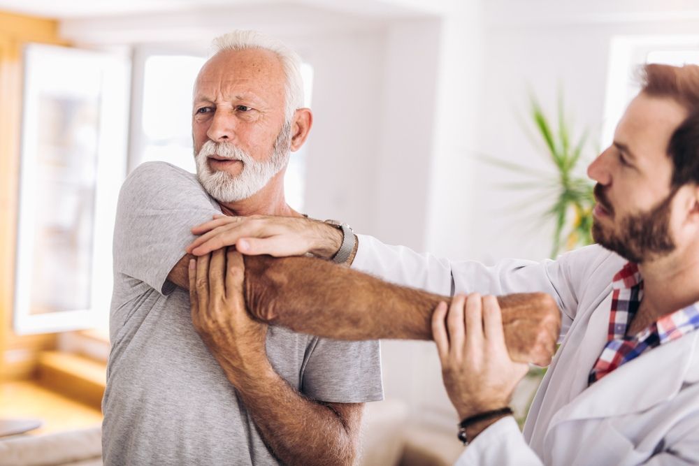 An Elderly Man is Being Helped by a Doctor to Stretch His Arms — One Stop Medical in Mackay, QLD