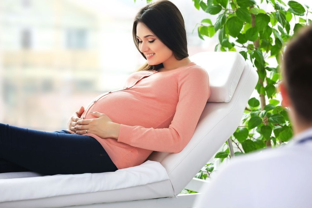 A Pregnant Woman is Laying on a Bed Talking to a Doctor — One Stop Medical in Mackay, QLD