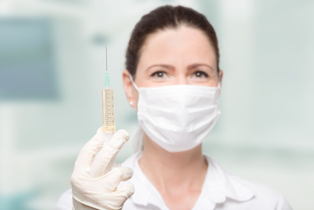 A Female Doctor Wearing a Mask and Gloves is Holding a Syringe — One Stop Medical in Mackay, QLD