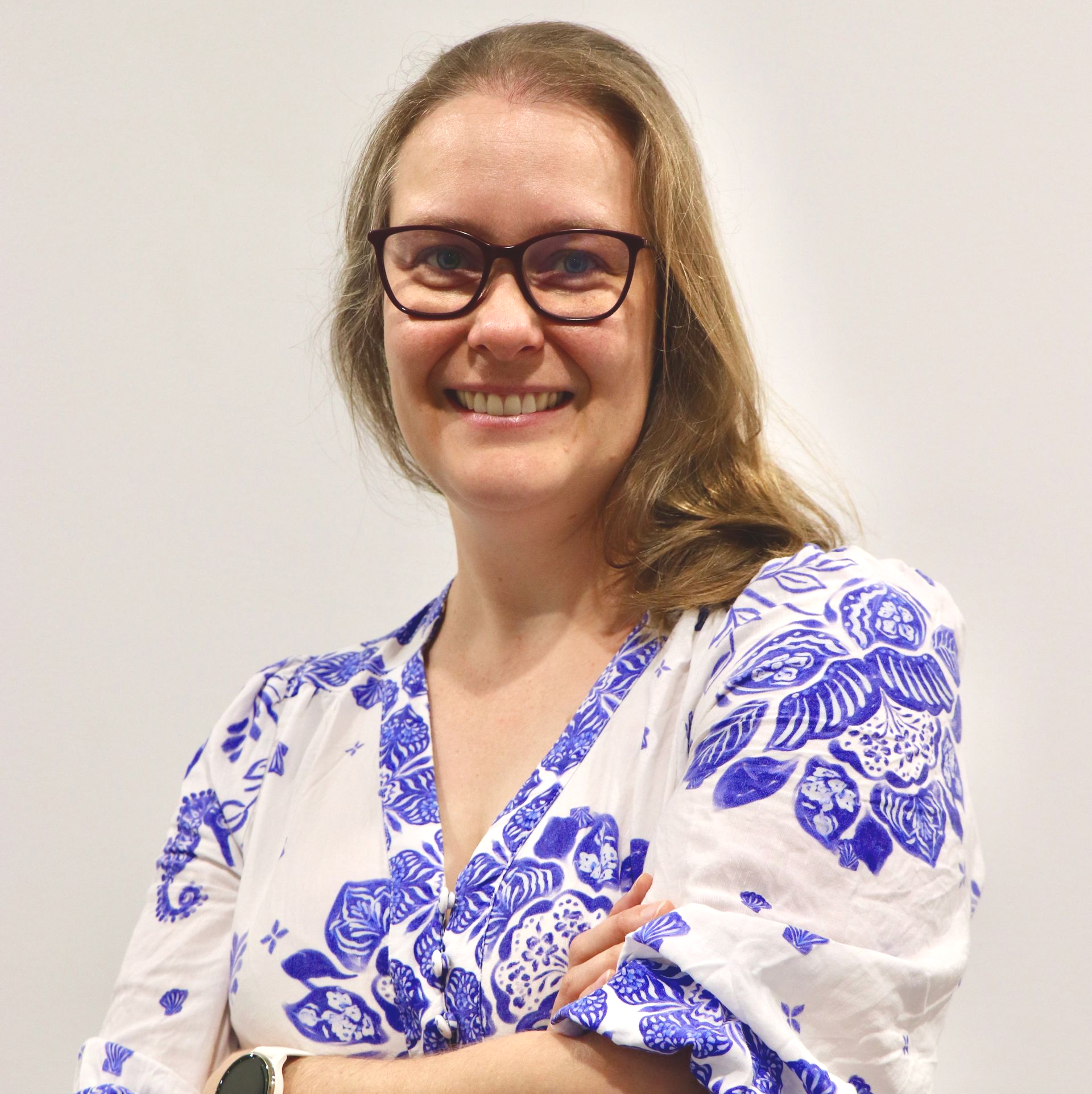 Woman in a blue and white floral dress with glasses, arms crossed, smiling — One Stop Medical in Mackay, QLD