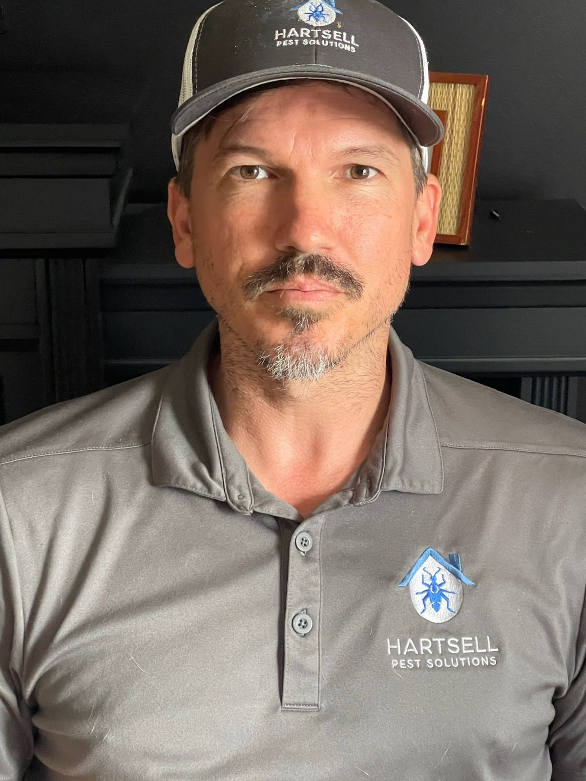Man wearing cap and polo shirt with company logo, looking forward.