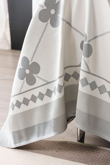 Plaid grigio chiaro con motivo floreale drappeggiato su una sedia su un pavimento ricoperto di moquette.
