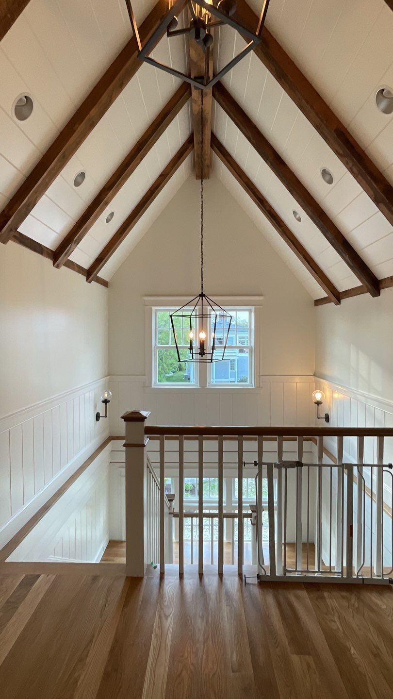 Wooden staircase with a high ceiling featuring exposed beams and a hanging chandelier.