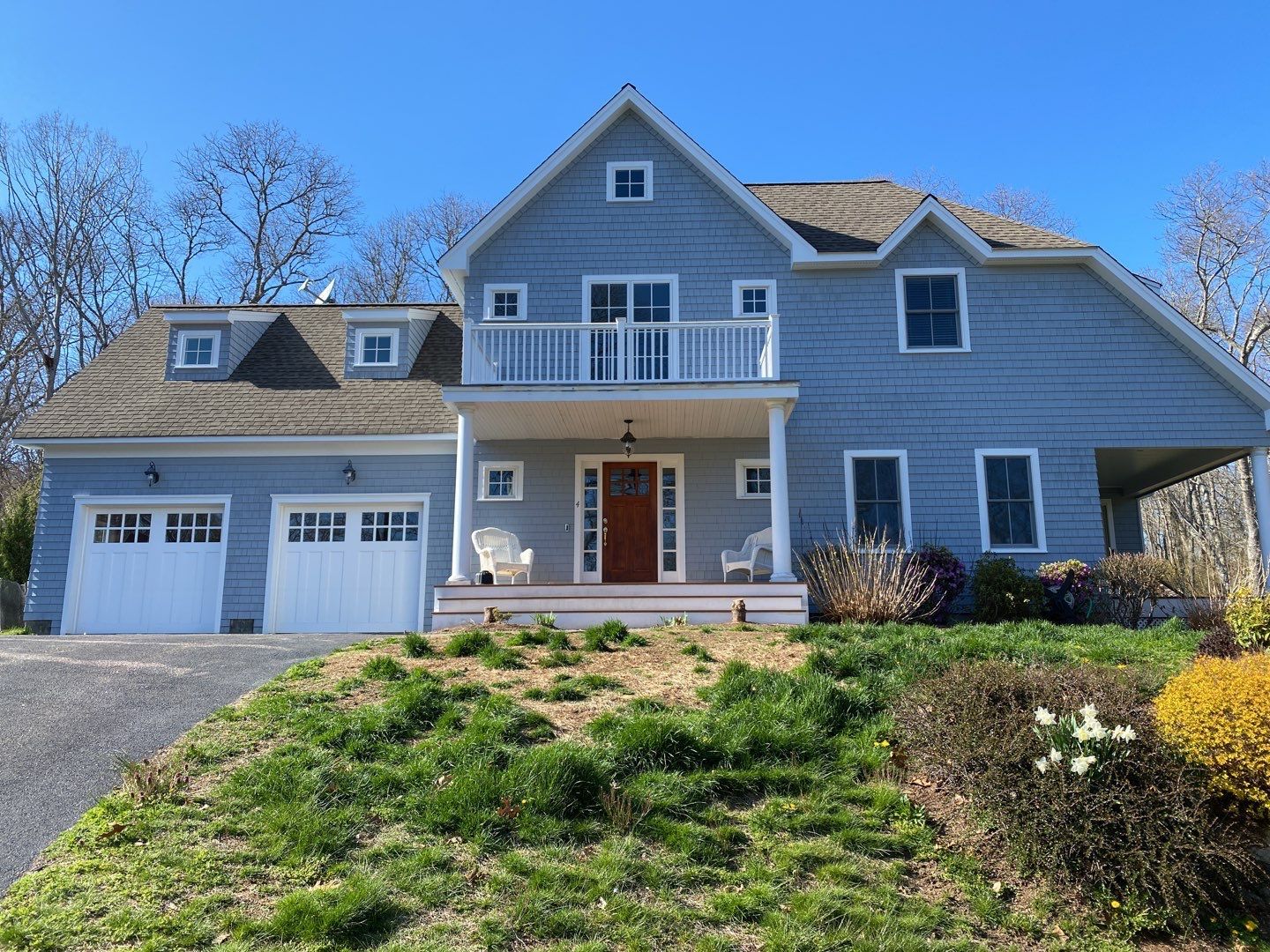 Blue house with white trim, two-car garage, and small porch. A grassy hill leads up to the home on a sunny day.
