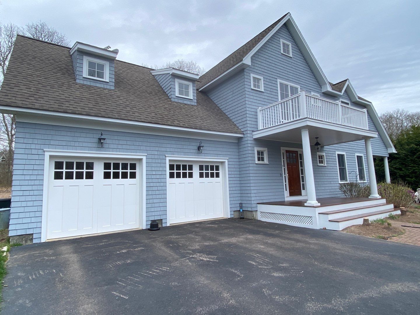 Blue house with white garage doors, balcony, and brown roof. Driveway leads up to the home.
