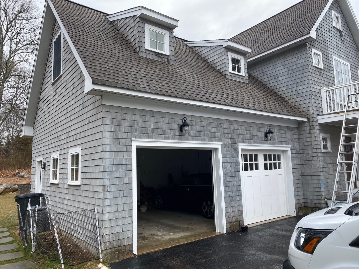 Two-story gray house with a two-car garage, white garage doors, dormer windows, and a car parked inside.