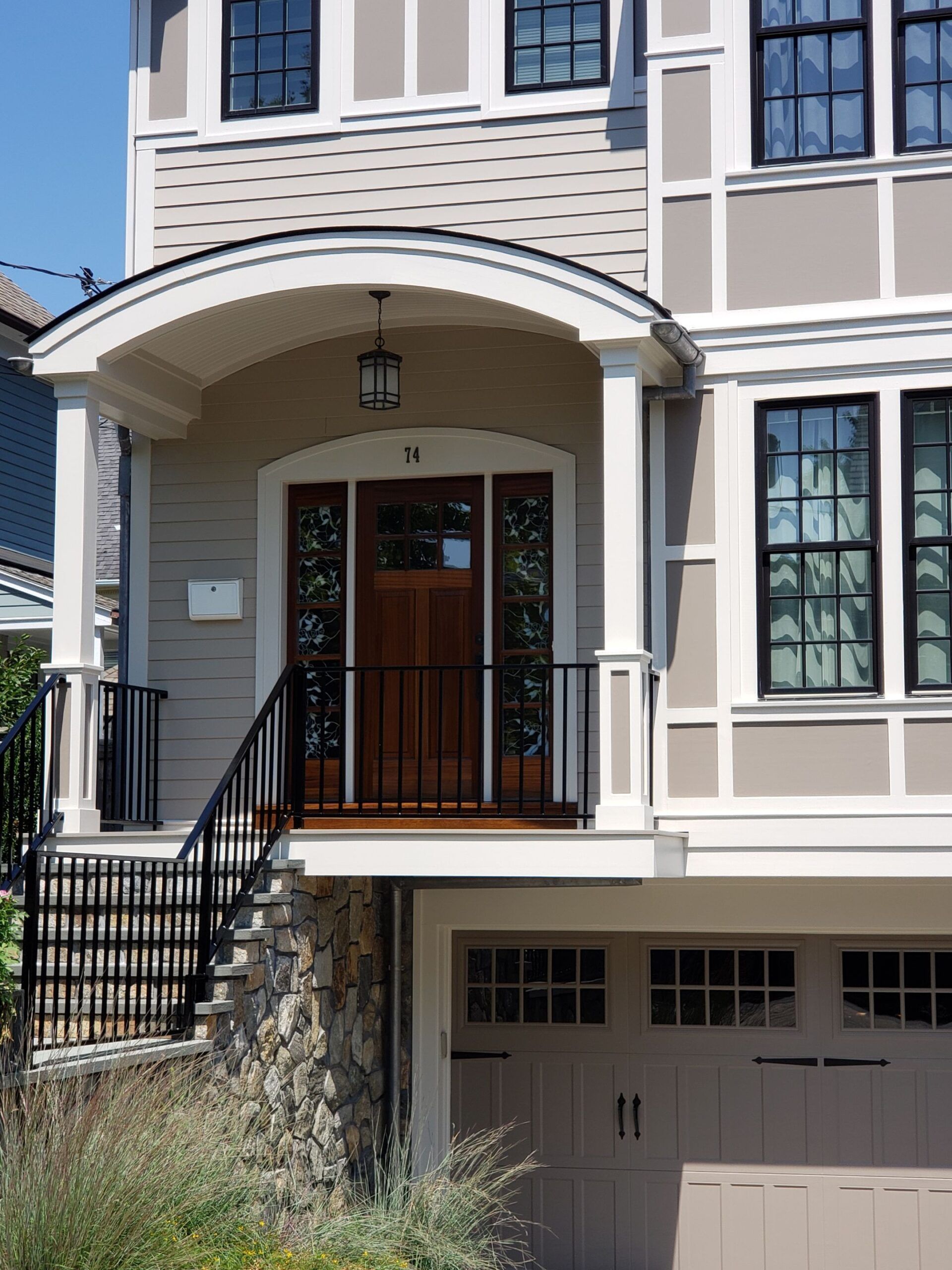 A two-story house with a stone foundation. A covered entryway has a dark brown door and black iron railing.