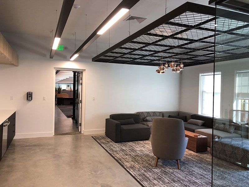 Modern office lounge area with a large gray sectional, armchairs, rug, and industrial-style lighting fixtures.