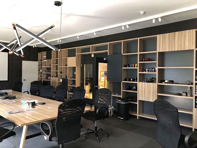 Conference room with a long wooden table, black chairs, and built-in wooden shelving on the back wall. The room has a modern design.