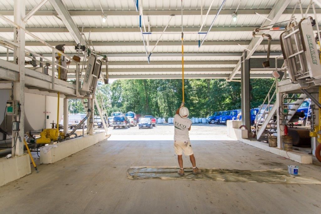 A worker in a factory setting pulls a cord, with equipment visible on either side and an open doorway leading to vehicles and trees.