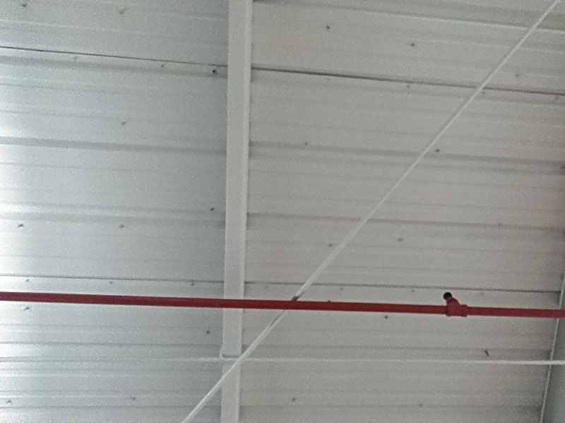 Red fire sprinkler pipe and white support beams against a corrugated metal ceiling.