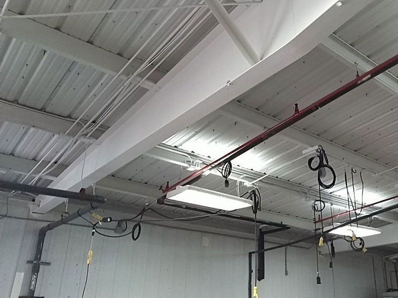 White gym ceiling with metal beams, pipes, and exercise rings hanging down. Overhead lights are also visible.