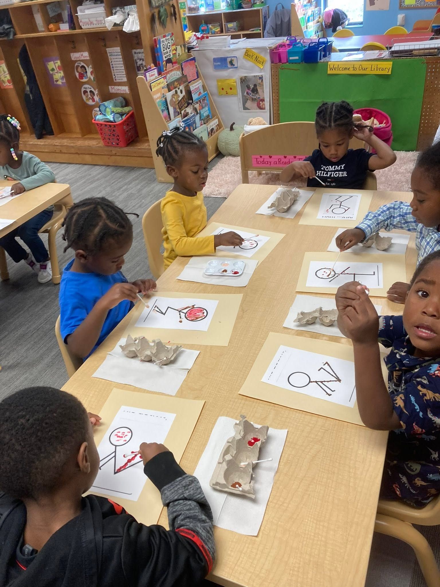 Children seated around a classroom table doing worksheet activities with crayons and manipulatives
